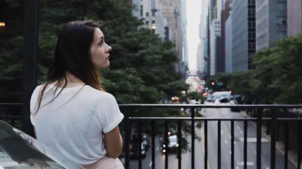 Вид сзади молодой красивой женщины, стоящей на мосту и смотрящей на проезжую часть в Нью-Йорке, Америка . — стоковое видео