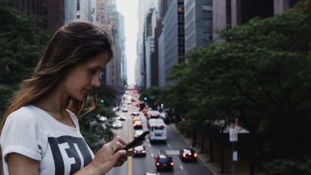 Porträt einer jungen schönen Frau, die auf der Brücke nahe der Verkehrsstraße in New York steht und das Smartphone benutzt. — Stockvideo