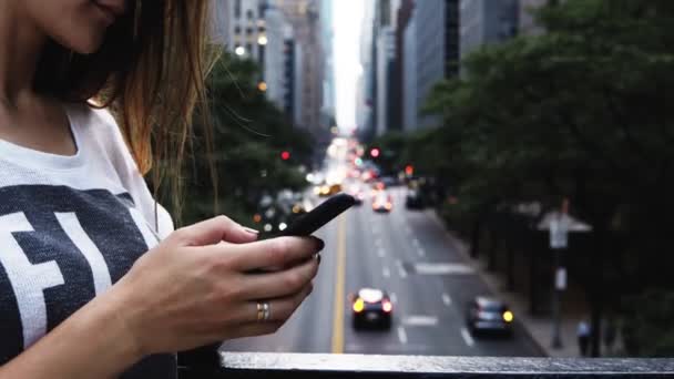 Vista de cerca de la mujer joven usando el teléfono inteligente, de pie en el puente cerca de la carretera de tráfico en Nueva York, Estados Unidos . — Vídeos de Stock