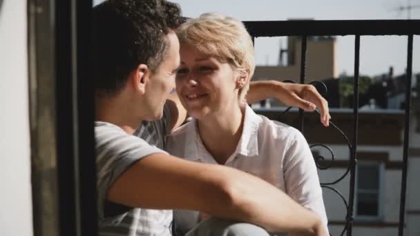 Belle jeune femme européenne assise près et parlant à son petit ami, touchant son nez et ses cheveux sur un petit balcon . — Video