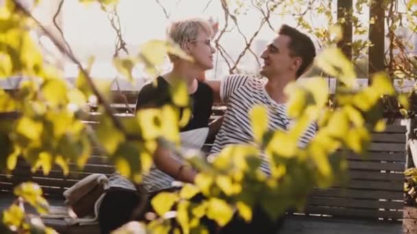 Ağır çekim tatlı romantik çift oturma birlikte eğleniyor ve güzel güneşli sonbahar günde bir bankta konuşuyor. — Stok video