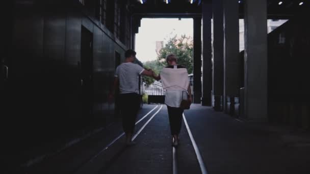 Slow motion bakåt Visa lyckliga romantiska paret gå tillsammans hålla händerna på skenor under mörk kväll city bridge. — Stockvideo