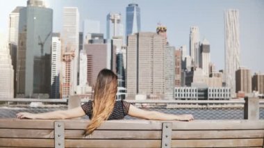 Arkadan görünüşü mutlu kız kollarını bankta oturan güzel Manhattan skyline New York'ta manzarayı uzun saçlı.