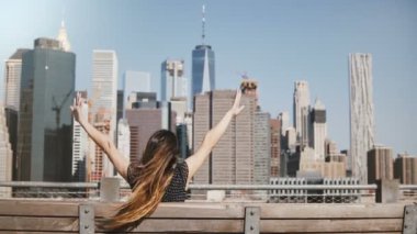 Uzun saçlı bir Bank üzerinde şaşırtıcı Manhattan skyline manzarayı rüzgarda üfleme mutlu kadın Gezgin görünümünü geri