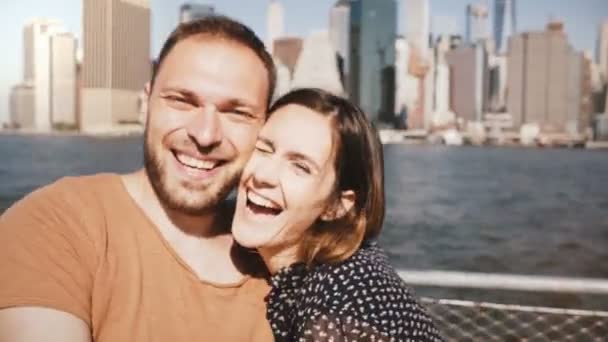 Feliz joven pareja sonriente posando para una foto selfie, besándose en la famosa vista del horizonte de Nueva York de los rascacielos de Manhattan . — Vídeo de stock