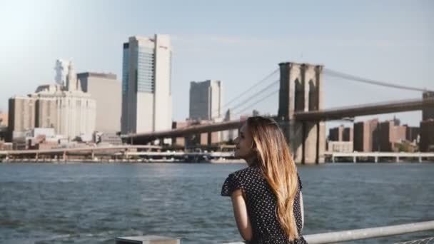 Pásztázás, boldog mosolygó európai nő a hajad élvezheti a híres New York-i skyline repülő és Brooklyn-híd nézet. — Stock videók