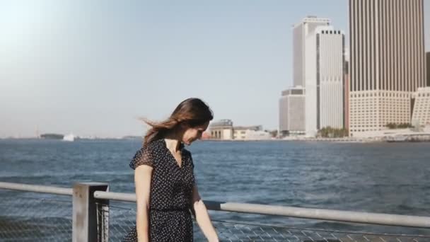 Bella donna caucasica sorridente con i capelli volanti passeggiando lungo il famoso skyline lungo il fiume del centro finanziario di New York — Video Stock