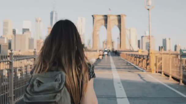Brooklyn Köprüsü, New York boyunca güzel güneşli yaz gününde 4 k yürüyüş sırt çantası ile genç kadın kamera izler. — Stok video