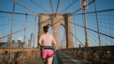 Brooklyn Köprüsü, New York boyunca sıcak yaz gününde çalışan iki yetişkin kadın. Bakış açısı düşük açılı açık gökyüzü 4k bir kadeh. İnanılmaz bir kentsel ortamda sağlıklı yaşam önde gelen çeşitli yaş insanlar.