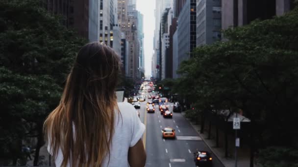 Вид сзади молодой стильной женщины, стоящей на мосту и смотрящей на проезжую часть в центре Нью-Йорка, Америка — стоковое видео