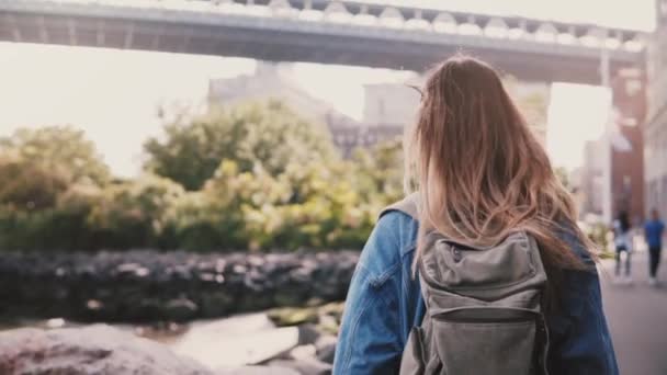 Genç kadın turist güneşli Brooklyn Park nehir setin ağır çekim yürüyüş sırt çantası kamera takip. — Stok video