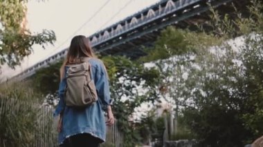 Genç gezgin kız güzel Brooklyn Bridge park ağaçlar yavaş hareket altında yürüyen sırt çantası ile düşük açılı çekim.