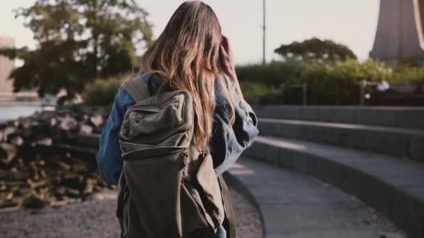 Camera follows beautiful Caucasian female tourist with backpack walking at Brooklyn Park concrete river bank slow motion — Stock Video