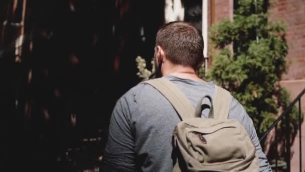 Cámara sigue joven hombre turístico relajado con mochila caminando a lo largo de verano sombreado calle de Nueva York con café . — Vídeo de stock