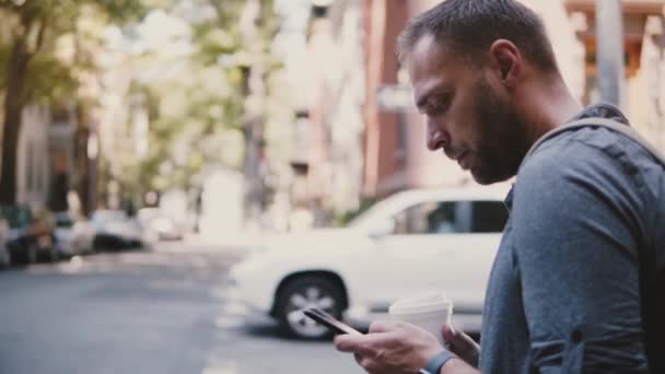 Magabiztos sikeres kaukázusi üzletember állandó város utca sarkán, kávéval, mobil irodai smartphone app segítségével — Stock videók