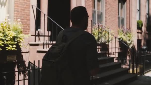 スマート フォン モバイル オフィス アプリケーションを使用してバックパックの日当たりの良い夏ニューヨークのブルックリンのストリートを歩いていると若い幸せな男. — ストック動画