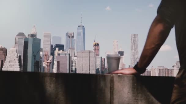 无法辨认的男性手拿着咖啡杯在难以置信的河岸边阳光明媚的曼哈顿, 纽约市的地平线全景 — 图库视频影像