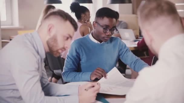 Twee multi-etnisch geconcentreerde jonge collega's werken op Gegevensanalyse in trendy loft kantoor, teamwork in de achtergrond. — Stockvideo