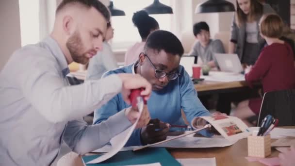 Two concentrated managers work through different papers and diagrams together by the table in modern multiethnic office. — Stock Video