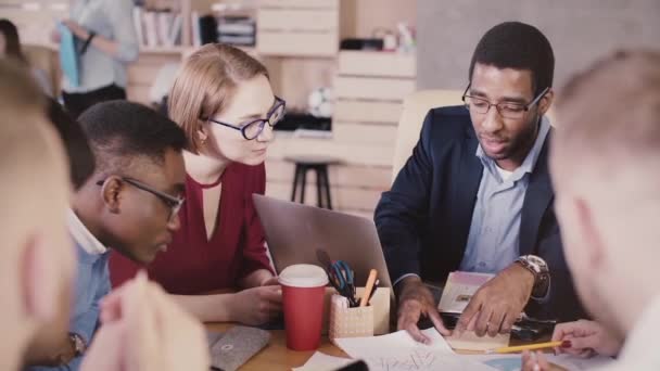 African American succesvolle mannelijke business coach leidt van multi-etnische office teamvergadering, tonen op grafieken op tafel. — Stockvideo