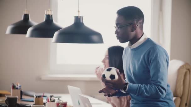 Афроамериканский бизнесмен сидит на рабочем столе, играет с небольшими футбольными переговорами с коллегой по замедленной съемке крупным планом . — стоковое видео