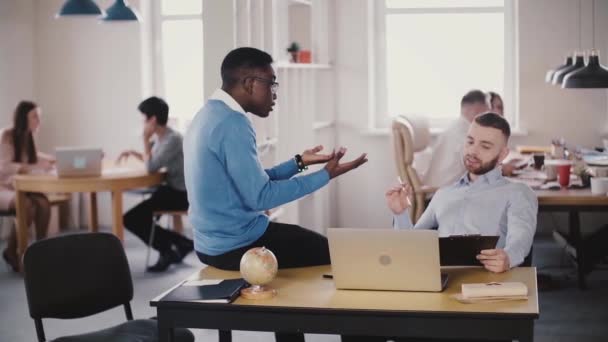Two young multiethnic friends talk, cooperate in modern healthy office. Colleagues discuss work, argue at workplace. — Stock Video