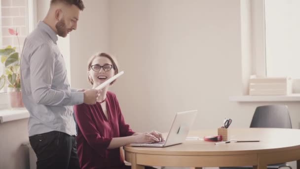 Jóvenes europeos cooperan junto a la mesa en la oficina moderna, hablan y sonríen. Trabajo en equipo en un lugar de trabajo saludable — Vídeos de Stock