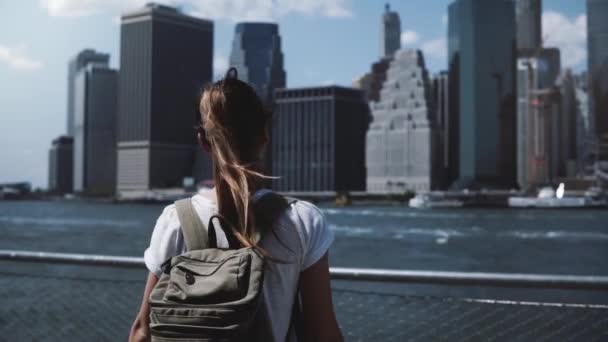 Bellissimo viaggiatore femminile con zaino alza le braccia aperte con eccitazione vicino allo skyline di Manhattan City a New York . — Video Stock