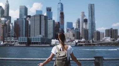Arkadan Görünüş sırt çantası ile genç mutlu turist kızın ve New York'ta meşhur Manhattan siluetinin sevinç ile geniş açık silah