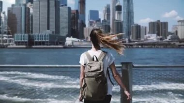 Kamera ile sırt çantası, Genç mutlu traveler kız New York'ta Manhattan siluetinin, geniş açık kollar ile atlama izler.