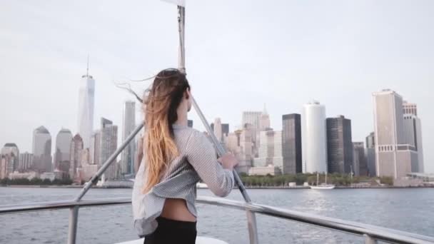 Belle fille voyageur excité avec les cheveux volants et les bras grands ouverts regarder New York skyline sur un bateau de visite au ralenti — Video