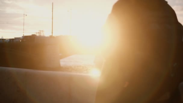 Joven y elegante hombre caminando por el terraplén al atardecer. Hombre solo pasando tiempo en la ciudad cerca del río . — Vídeo de stock