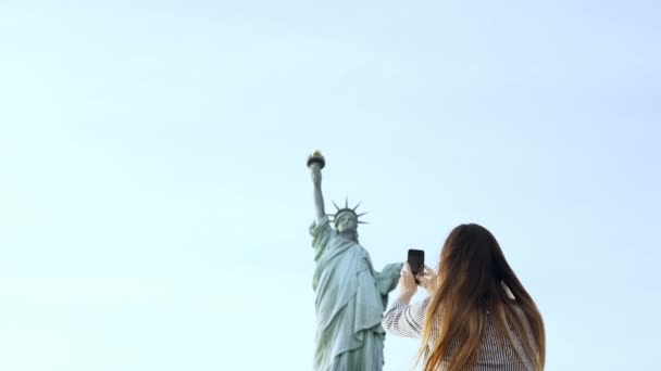 Vackra leende Europeiska turist kvinna tar en smartphone foto av Frihetsgudinnan i New York City, vänder sig till kameran — Stockvideo