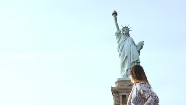 Feliz atractiva y sonriente turista europea hablando por teléfono en la Estatua de la Libertad en Nueva York en un día soleado . — Vídeos de Stock