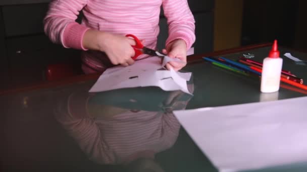 Close-up shot van schattige kleine meisjes handen in roze trui kapvormen van papier, glazen tafel als gevolg van haar gezicht. — Stockvideo