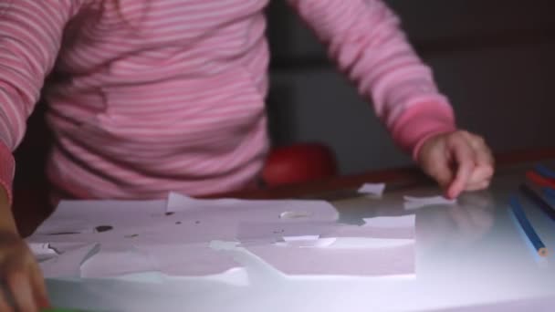 Primer plano de las niñas manos en suéter rosa corte formas de hoja de papel con tijeras en una mesa de vidrio . — Vídeos de Stock