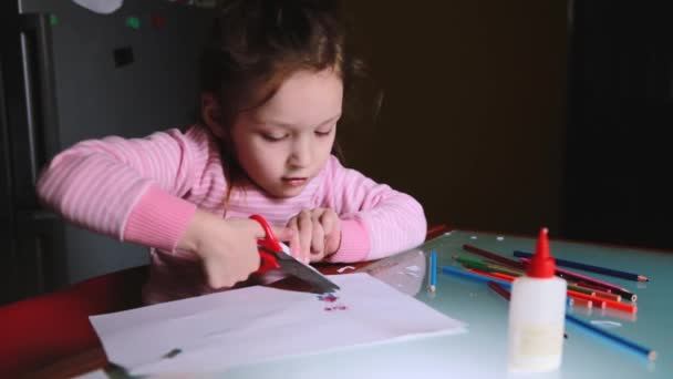 Cute little preschool European girl child in pink sweater cutting her drawing out of paper sheet, talking to someone. — Stock Video