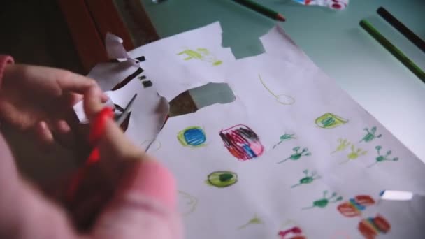 特写镜头的可爱的小女孩的手切割 handdrawn 图片从纸页与剪刀在桌子上. — 图库视频影像