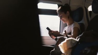 Güzel mutlu beyaz kız trende seyahat ederken gülümseyen ve smartphone kullanarak arkadaşlarınızla iletişim.