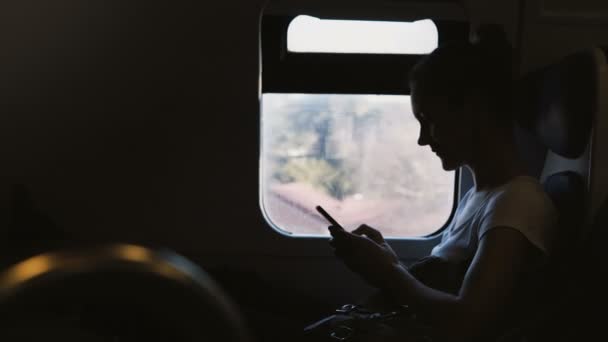 Σκοτεινή σιλουέτα νεαρό θηλυκό αμαξοστοιχίας επιβάτη χρησιμοποιώντας messenger εφαρμογή για smartphone, ενώ κάθεται στο κάθισμα παραθύρων. — Αρχείο Βίντεο