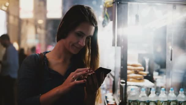 Felice attraente CEO femminile utilizzando smartphone e-commerce app vicino fumante venditore di street food in serata New York City . — Video Stock