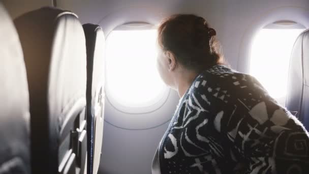 Passagère européenne âgée assise sur le siège de la fenêtre de l'avion, nerveuse et effrayée à l'idée de voler, regardant autour de elle — Video