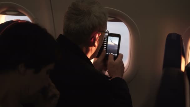 Oigenkännlig senior manlig passagerare tar smartphone foto av plan vinge under flygning sitter nära flygplan fönster. — Stockvideo