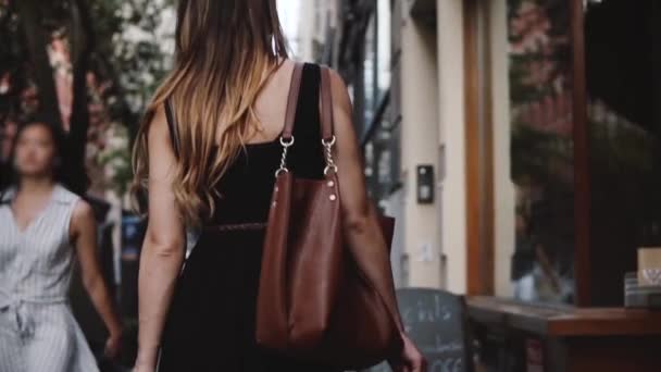 Kamera verfolgt junge Modebloggerin mit stylischer Tasche beim Spazierengehen entlang der schönen kleinen Stadtstraße in Zeitlupe. — Stockvideo