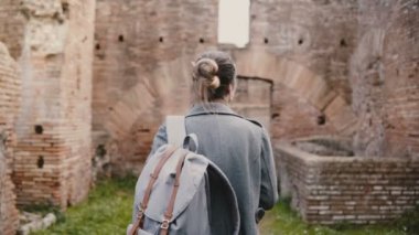Arkadan Görünüş sırt çantası ile heyecanlı genç kız öğrencinin araştırmacı ve Ostia, İtalya için antik kalıntıları keşfetmek göster.