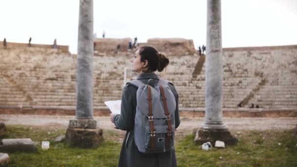 Achteraanzicht van mooie jonge vrouwelijke toerist met rugzak en kaart verkennen oude amfitheater ruïnes in Ostia, Italië. — Stockvideo