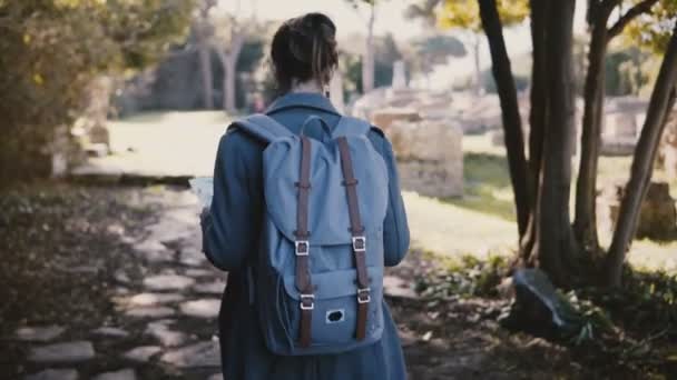 Vista posterior de la joven mujer feliz con mochila caminando con un mapa a lo largo de ruinas antiguas en Ostia Antica, Italia de vacaciones . — Vídeo de stock