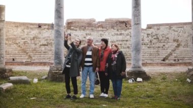 Genç Avrupa kız ve Ostia, İtalya için eski amfitiyatro ruins yakınındaki selfie alarak mutlu üst düzey turist grup gülümseyen.