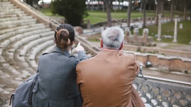 Veduta posteriore del padre e della figlia europei seduti a parlare alle vecchie rovine dell'antico anfiteatro di Ostia in Italia . — Video Stock