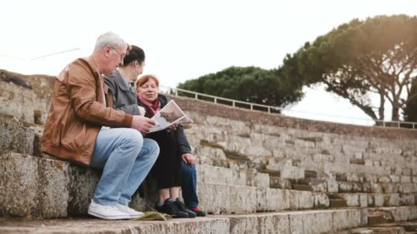 Lycklig kaukasiska senior familj med unga dotter sitter och pratar på amfiteatern ruinerna i Ostia, Italien med en karta. — Stockvideo